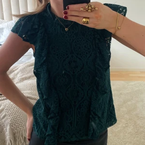 Grön blus - Superfin mörkgrön blus med volanger och spets. Knapp i nacken. Bra skick!