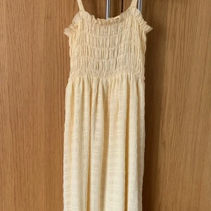 Ljusgul sommarklänning från Monki - Supersöt ljusgul klänning från Monki med smock upptill, volangdetaljer vid axlarna och knytning i ryggen. Klänningen har tunna axelband och är tillverkad i ett lätt, strukturerat tyg – perfekt för varma dagar. Endast använd några få gånger. Skriv för fler bilder!💕🌺☀️ 