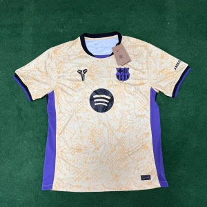 FC Barcelona bortatröja 2025/26 - Säljer en FC Barcelona bortatröja från Nike i guld/beige med lila detaljer. Tröjan har korta ärmar, svart krage och klubbmärke på bröstet. Sponsorer som Spotify och UNHCR syns tydligt. Perfekt för dig som älskar Barca!
