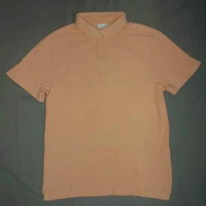 Beige pikétröja med krage - Säljer en stilren beige pikétröja med klassisk krage och knäppning framtill. Tröjan har korta ärmar och är perfekt för en avslappnad men ändå snygg look.