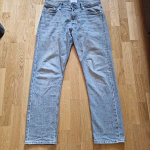 Grå jeans från Jack & Jones - Säljer ett par klassiska grå jeans från Jack & Jones med raka ben och fem fickor. Jeansen har normal passform och stängs med dragkedja och knapp. Perfekta till vardags för en stilren look.