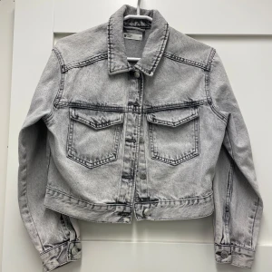 Grå jeansjacka från Gins Tricot - perfect jeans - Säljer en snygg grå jeansjacka från Gina Tricot, g perfect jeans i storlek XS. Jackan har en klassisk krage och knappar framtill. Kort modell, två bröstfickor fram med lock. Perfekt för en cool och avslappnad stil.