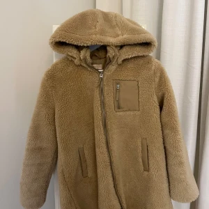 Beige teddyjacka från Kids Only - Mysig beige teddyjacka från Kids Only med huva och dragkedja framtill. Jackan har två fickor och en bröstficka med dragkedja. Jackan är knappt använd och är i nyskick. Storlek 146-152 men ganska stor i storleken så den passar typ XS❤️