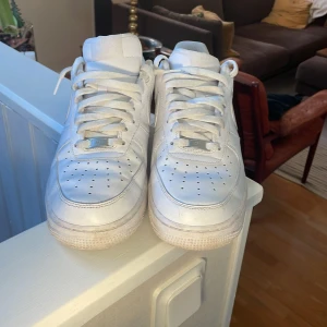 Vita Nike Air Force sneakers - Säljer ett par klassiska vita Nike Air Force sneakers. Skorna har en stilren design med snörning och perforerade detaljer på tån för extra ventilation. Perfekta för en casual look.