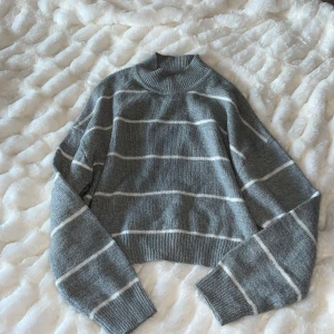 Grå och vit randig tröja från H&M Divided - Säljer en stilren grå tröja med vita ränder från H&M Divided. Tröjan är stickad och har en normal passform med långa ärmar och ribbade kanter. Perfekt för kyligare dagar. Gråblå med vita ränder