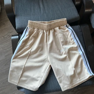 Beige shorts med ränder - Snygga beige shorts med elastisk midja och vita samt svarta ränder längs sidorna. Perfekta för en avslappnad stil.