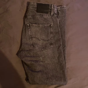 Grå jeans från Jack & Jones - Säljer ett par grå jeans från Jack & Jones i modellen Relaxed/Chris. De har en avslappnad passform med knappar i gylfen och klassiska fem fickor. Perfekta för en casual look. priset ej hugget i sten!
