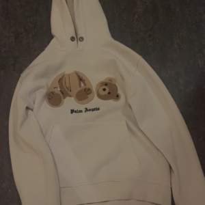 Säljer en vit hoodie från Palm Angels med ett unikt nallemotiv på framsidan. Hoodien har en klassisk design med dragsko i huvan och ribbade muddar vid ärmslut och nederkant. Perfekt för en avslappnad stil.