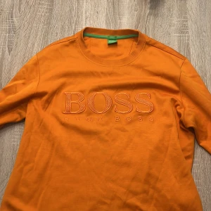 Orange tröja från Hugo Boss - Säljer en snygg orange tröja från Hugo Boss med broderad logga på framsidan. Tröjan har en slim fit passform och rund halsringning. Perfekt för att liva upp garderoben med lite färg! (OBS STRL L men passar M personer bättre, slim fit modell)