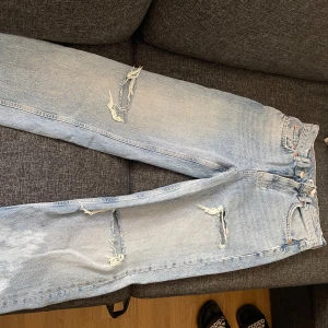 Ljusa jeans med slitningar - Snygga ljusa jeans med slitningar på framsidan. De har en klassisk femficksdesign och knappar i midjan. Perfekta för en avslappnad stil. Aldrig använda. 