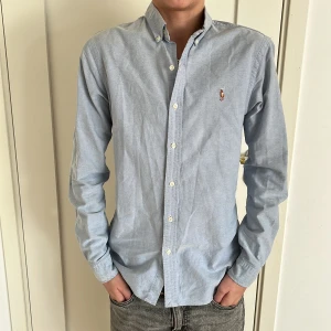 Blå skjorta från Ralph Lauren - Säljer en stilren blå skjorta från Ralph Lauren i slim fit. Skjortan har långa ärmar och knappar framtill samt en broderad logotyp på bröstet 