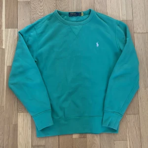 Grön sweatshirt från Polo Ralph Lauren - Säljer denna stilrena sweatshirt från Polo Ralph Lauren med det klassiska broderade logotypen på bröstet. Tröjan har långa ärmar och ribbade muddar vid ärmslut och nederkant. Perfekt för en avslappnad look.