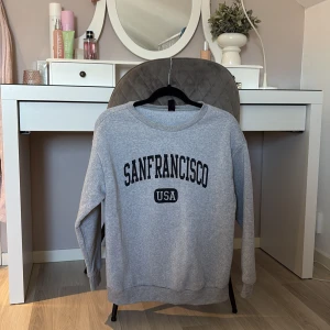 Grå sweatshirt med San Francisco-tryck - Säljer en grå sweatshirt med texten 'San Francisco USA' tryckt på framsidan. Tröjan har en rund hals och långa ärmar, perfekt för en avslappnad stil. Passar bra till jeans eller leggings för en casual look. Är även en over sized tröja❤️