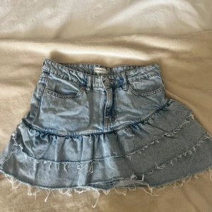 Blå jeanskjol med volanger - Snygg blå jeanskjol med volanger. Är använd men väldigt fint skick. Storlek 34.