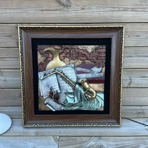 Tavla med musikinstrumentmotiv - Säljer en dekorativ tavla med ett motiv av musikinstrument och noter. Tavlan har en elegant träram med detaljerade guldfärgade ornament. Perfekt för musikälskare som vill ha en konstnärlig touch i hemmet.