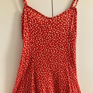 Röd blommig klänning - Säljer en söt röd klänning med vita blommor. Klänningen har smala axelband och en lätt utsvängd kjol. Även en söt liten detalj bak på ryggen som du kan reglera!💗Säljer då den aldrig kommit till användning! För fler bilder kom privat💗 Pris kan diskuteras!