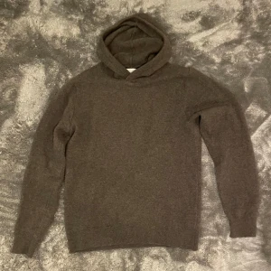 Grå lite mörkgrön hoodie i merinoull från Vailent - Säljer en stilren grå lite mörkgrön  hoodie från Vailent i mjuk merinoull. Perfekt för kyliga dagar med sin sköna passform och långa ärmar. Huvan ger extra värme och stil. Passar både till vardags och mer avslappnade tillfällen. Den är i storlek S och 100% merinoull. 