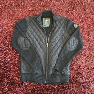 Marinblå quiltad cardigan från State of Art - Snygg svart quiltad jacka från State of Art med dragkedja och ribbade detaljer. Jackan har långärmade ärmar och quiltade armbågslappar. Perfekt för en stilren look. Använd bara några få gånger. Mycket bra skick.