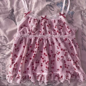 Rosa blommig linne med spetsdetaljer - Söt rosa linne med körsbärsmönster och spetsdetaljer. Den har smala axelband och små rosetter framtill. Perfekt för en somrig look! Köpt i usa.