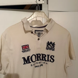 Beige pikétröja från Morris  - Säljer en stilren beige pikétröja från Morris Gent's med broderade detaljer och en klassisk krage. Tröjan har korta ärmar och en knappslå framtill. Perfekt för en avslappnad men ändå snygg look.