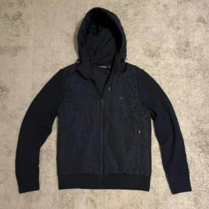 J.Lindeberg Cardigen - Snygg  blå jacka ifrån J.Lindeberg. Inga synliga defekter bara ett hål i vänstra fickan som man ej ser eller märker av. Dragkedjan har tappat lite färg om man kollar noga men åter igen inget man märker. 