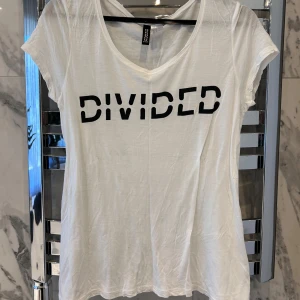 Vit t-shirt frn H&M - Säljer en vit t-shirt från Divided by H&M med trycket 'DIVIDED' i svart på framsidan. Storlek 38, köparen står för frakten!❤️