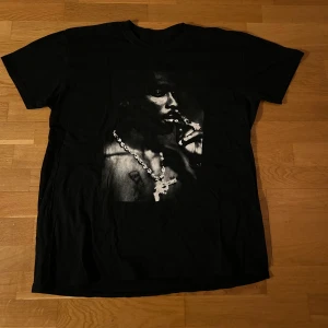 Svart oversized T-shirt med 2Pac-tryck - Säljer en svart oversized T-shirt med ett coolt tryck av 2Pac. Perfekt för dig som vill ha en stilren och ikonisk look. T-shirten har korta ärmar och en normal passform. Ett måste för alla hiphop-fans! Passar även L och XL