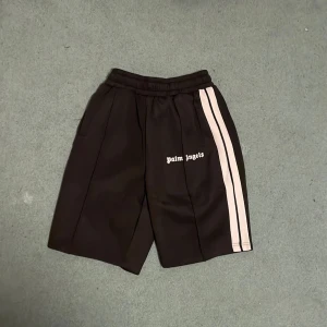 Svarta shorts från Palm Angels - Snygga svarta shorts från Palm Angels med vita ränder längs sidorna. De har en elastisk midja för extra komfort och stilren design med logotypen tryckt på framsidan. Perfekta för en avslappnad look.Storlek M men passar L