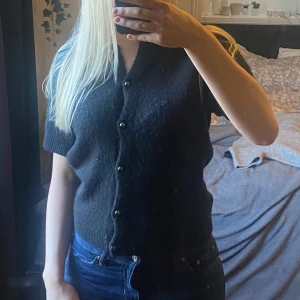 Svart stickad kortärmad med knappar från Gina Tricot - Säljer en svart kortärmad kofta från Gina Tricot. Koftan har knappar framtill och är perfekt för lager-på-lager-stil. Den är gjord i ett mjukt material som känns skönt mot huden.