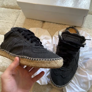 Maison Margiela - Unika svarta sneakers från Maison Margiela med en rå och avslappnad design. Skorna har en synlig söm och en sula i naturmaterial som ger en bohemisk känsla. Perfekta för dig som vill ha något annorlunda och stilrent. Passar mindre 42-44