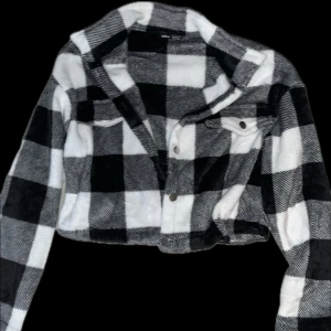 Svartvit rutig croppad jacka - Snygg svartvit rutig jacka med croppad passform. Jackan har långa ärmar och knappar framtill. Perfekt för en trendig look.