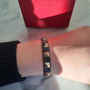 Valentino Armband - Valentino Rockstud Armband. Självklart äkta✅️Riktigt snyggt armband som kan justeras. Bra skick! Lite skada längst ut på armbandet syns på bild 3 men det kan enkelt fixas med lite lim. Allt medkommer vid köp, såsom extra nitar, valentino tygpåse, extra läder samt ett valentino kort.
