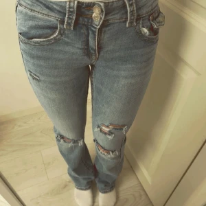 Låg midjade bootcut Blå jeans med slitningar - Snygga blå jeans med slitningar på knäna och låren. De har en klassisk femficksdesign och knappar i midjan💕💕Skriv för flera bilder! Har sytt jeansen där bak!!‼️är 162cm lång!!😊😊😊 storlek 158🥰🥰