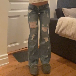 Lågmidjade bootcut jeans med slitningar - Säljer dessa ljusblå jeans som är utsydda till bootcut med slitningar. Midjemått 36 cm tvärs över och de är bra i längd på mig som är 163 cm lång. Kontakta mig gärna privat vid frågor eller liknande💓