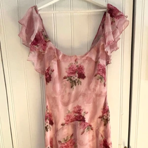 Rosa blommig klänning från ASOS DESIGN - Säljer en romantisk rosa klänning från ASOS DESIGN med blommigt mönster. Klänningen har volangdetaljer. Perfekt för sommarens festligheter. Den har en luftig och fladdrig design som ger en feminin touch.