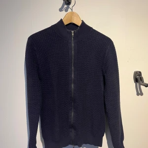 Mörkblå stickad kofta från John Henric - Snygg mörkblå stickad kofta från John Henric med dragkedja. Perfekt för vår/sommar. Den sitter slim fit och har ribbade ärmar och krage. Använd en del, men fortfarande bra skick. Passar ca. 180. Hör av er vid frågor! 