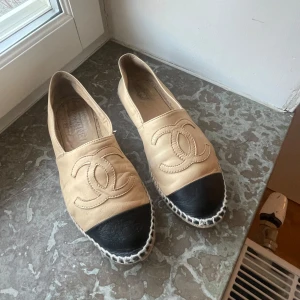 Beige och svarta espadrillos från Chanel - Snygga espadrillos från Chanel i beige skinn med svart tå och flätad sula. Köptes i Chanel butiken i New York för 4 år sen och tyvärr hittar jag inte kvittot, dem är väl använda där av priset. Storlek 38. Nypris 10 480kr. Pris kan diskuteras!