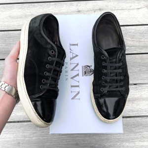 Svarta sneakers från Lanvin - Snygga svarta sneakers från Lanvin med en kombination av mocka och skinn. Skorna har en vit sula och snörning framtill. Perfekta för en stilren look.