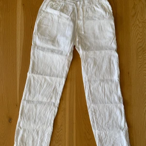 Vita linnebyxor från Woodbird - Säljer ett par vita linnebyxor från Woodbird i storlek M. Byxorna har en avslappnad passform med elastisk midja och dragsko för justering. Perfekta för varma dagar med sitt lätta och luftiga material. Nypris 1000kr och mitt 200kr!!!!