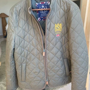Olivgrön quiltad jacka från Morris - Säljer en olivgrön quiltad jacka från Morris med broderad logga och brittisk flagga på bröstet. Jackan har dragkedja framtill och långa ärmar. Perfekt för höst och vår. Jackan är i absolut nyskick utan defekter Nypriset ligger på 2300 och nu säljer jag för 650 kr hör av er vid minsta fundering först till kvarn gäller mvh Ernstwarderobe🤝✅