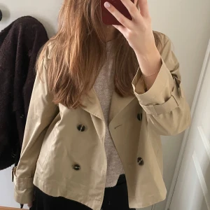 Beige trenchcoat med knappar - Snygg beige trenchcoat med dubbelknäppning och klassisk krage. Jackan har långa ärmar med justerbara remmar vid ärmsluten och två framfickor. Perfekt för vår och höst! Storlek M men skulle säga S. Prislapp kvar!