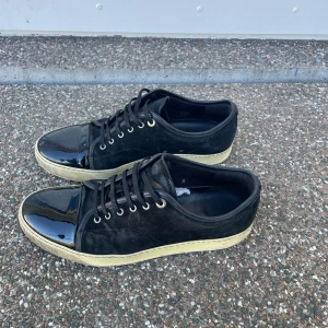 Lanvin DBB1 Patent Cap Toe  - Snygga svarta sneakers med en glansig tå och snörning. Skorna har en kontrasterande vit sula som ger en cool look. Perfekta för en stilren vardagsstil. Pris kan diskuteras vid snabbt affär! Nypris:4999kr 
