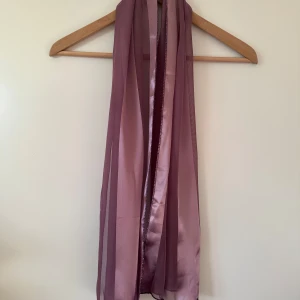 Ljuslila sjal i satin - Elegant sjal i en vacker lila nyans. Sjalen har ett randigt mönster med skira och blanka partier, vilket ger en fin textur och lyster. Perfekt till ditt nya vår-jag. Mycket gott skick.   Hämtas i Stockholm eller skickas mot porto. 