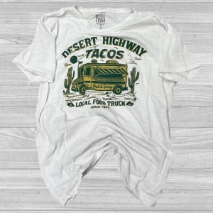 MudoFTS64 - Säljer en vit t-shirt från Mudo med ett coolt tryck av en food truck och texten 'Desert Highway Tacos'. Perfekt för en avslappnad stil. T-shirten har korta ärmar och är gjord i bomull.