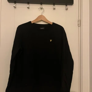 Svart tröja från Lyle & Scott - Säljer en stilren svart tröja från Lyle & Scott med deras ikoniska gula logga på bröstet. Tröjan har långa ärmar och en rund halsringning. Hör av dig vid funderingar!