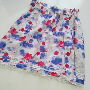 Blommig kjol från Pepe Jeans - Säljer en söt blommig kjol från Pepe Jeans. Kjolen har ett färgglatt mönster med röda och blå blommor på en vit bakgrund. Den är gjord av 100% silke och har en fin spetsdetalj längst ner. Perfekt för en somrig look! (L = 47 cm)