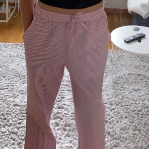 Rosa randiga byxor med snörning - Snygga rosa byxor med vita ränder och bekväm snörning i midjan. Perfekta för en avslappnad stil. Byxorna har en loose passform och är tillverkade i ett mjukt material. Jag har även ett par likadana fast ljusblå istället för rosa som jag säljer💕