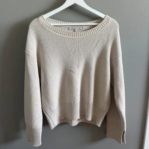 Beige stickad tröja House of Lola - Supermysig beige stickad tröja från House of Lola med bred ribbad kant och slits vid ärmsluten. Tröjan har en loose fit och offshoulder-look som ger en chill vibe. Perfekt till jeans eller leggings för en avslappnad stil.