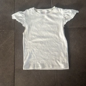 Vit blus med spetsärmar Gina Tricot - Supersöt vit blus från Gina Tricot i storlek 158/164. Toppen har korta ärmar i broderad spets med volangkänsla och en ribbad kropp i mjuk bomull.❤️