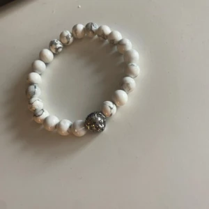 Vitt pärlarmband med lejonhuvud - Snyggt armband med vita marmorerade pärlor och en cool silverfärgad lejonhuvud-detalj. Elastiskt band gör det enkelt att ta på och av. Perfekt accessoar för att ge din outfit lite edge.